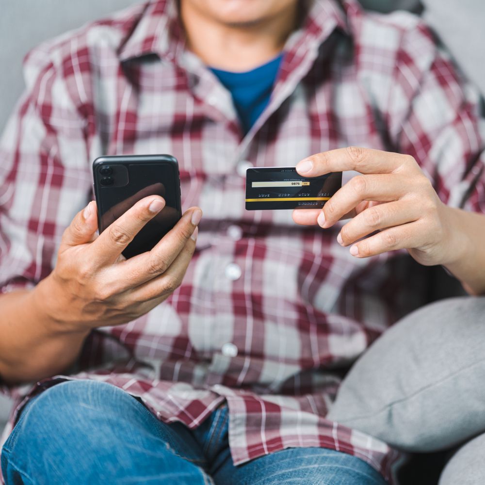 Guide to online shopping payment: Man in a plaid shirt entering credit card details on a smartphone for an online purchase.