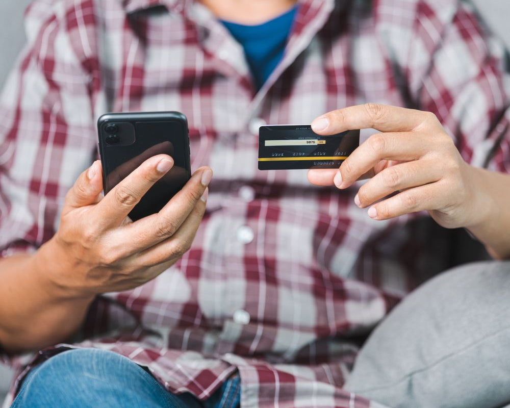 Guide to online shopping payment: Man in a plaid shirt entering credit card details on a smartphone for an online purchase.