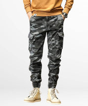 A fashion-forward outfit featuring men's grey camouflage cargo pants with a mustard sweater and cream boots.