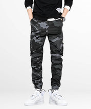 Front view of a man standing in black and gray camo cargo pants, featuring the pants' sleek design and cargo pockets.