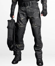 Man carrying a black combat carry bag while wearing black camo combat pants, designed for tactical and outdoor use.
