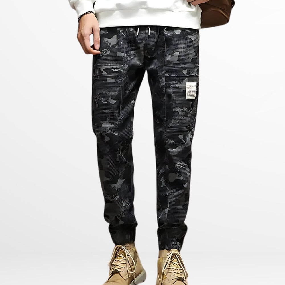 Man in black and grey camo cargo pants paired with tan boots, front view showcasing urban style and fit.