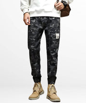 Man in black and grey camo cargo pants paired with tan boots, front view showcasing urban style and fit.