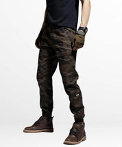 Side view of a man in brown camouflage pants with hands on hips, casual pose.