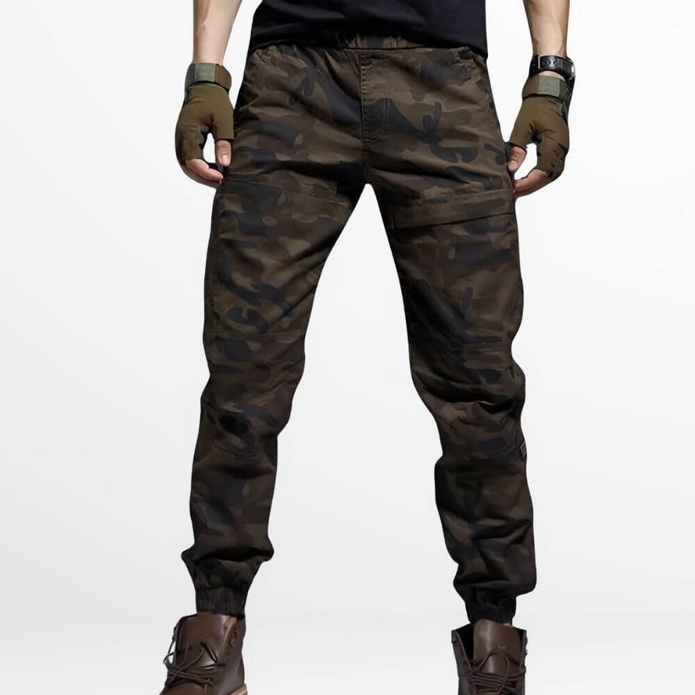 Man in brown camouflage pants standing with hands in pockets, front view.