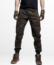 Man in brown camouflage pants standing with hands in pockets, front view.
