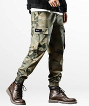 Side view of camo green cargo pants for men, showing detailed side pocket and styled with brown leather boots.