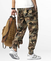 Side view of a person dressed in stylish camouflage cargo pants with a brown leather backpack, highlighting a modern urban fashion ensemble.