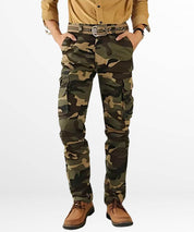 A casual stance in cargo pants for men in a camo pattern, matched with tan shoes and a mustard shirt for a cohesive earth-tone outfit.