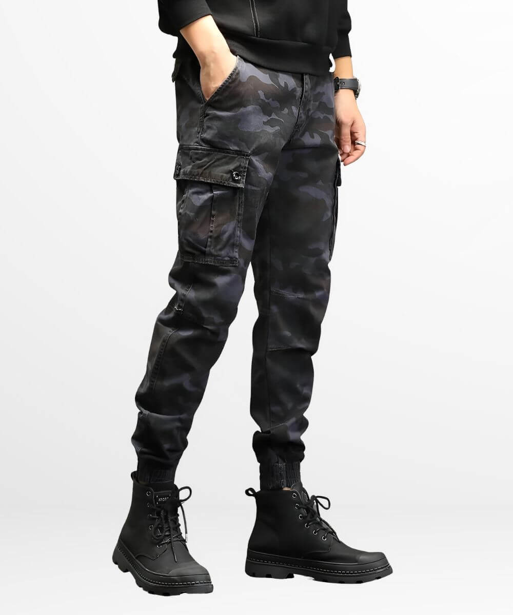 Side view of a man in dark grey camo cargo slim-fit pants showing utility pockets and tapered leg fit, paired with high-top black boots.