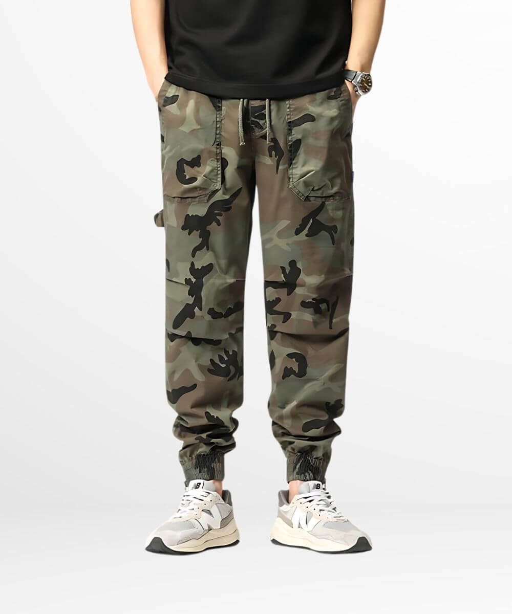 A person standing in a pair of green camo cargo sweatpants paired with chunky white sneakers and a black shirt, highlighting a casual yet fashionable streetwear outfit.