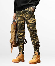 A model showcasing khaki camo cargo jogger pants paired with classic tan work boots, accessorized with a matching backpack for a cohesive outdoor look.