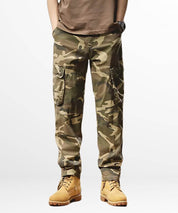 Model showcasing a pair of khaki camo cargo pants with multiple pockets and a modern, tactical design.