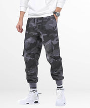 Man in a casual stance wearing men's baggy grey camo cargo pants with hands in pockets, showcasing a relaxed and stylish fit.