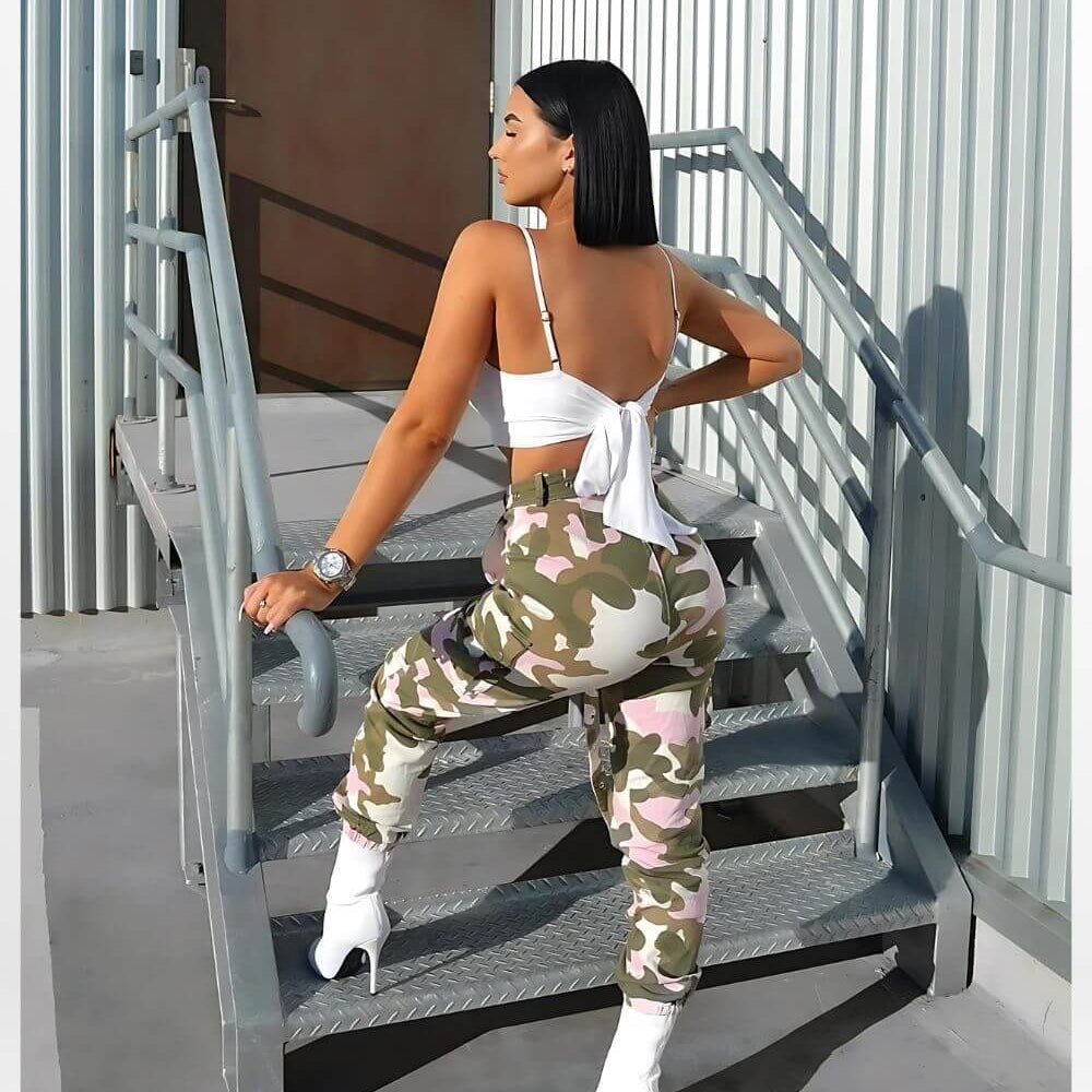 Stylish back view of woman in pink camouflage pants and white boots on industrial stairs, streetwear fashion.