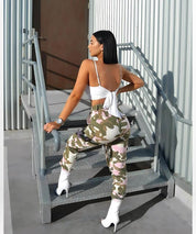 Stylish back view of woman in pink camouflage pants and white boots on industrial stairs, streetwear fashion.