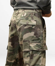 Side angle focusing on the pocket detail of green baggy camo pants, accentuating the practical design.