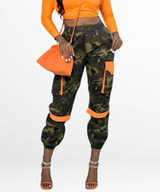Fashionable women's camo pants with vibrant orange accents, styled with high heels and a matching clutch for a chic look.