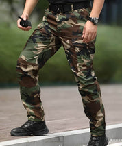 Close-up of woodland camo military cargo pants with a model holding a tactical device, featuring durable fabric and tactical belt.