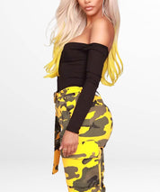 Three-quarter rear view of a woman showcasing the fit of yellow camo pants with a tied waist belt.